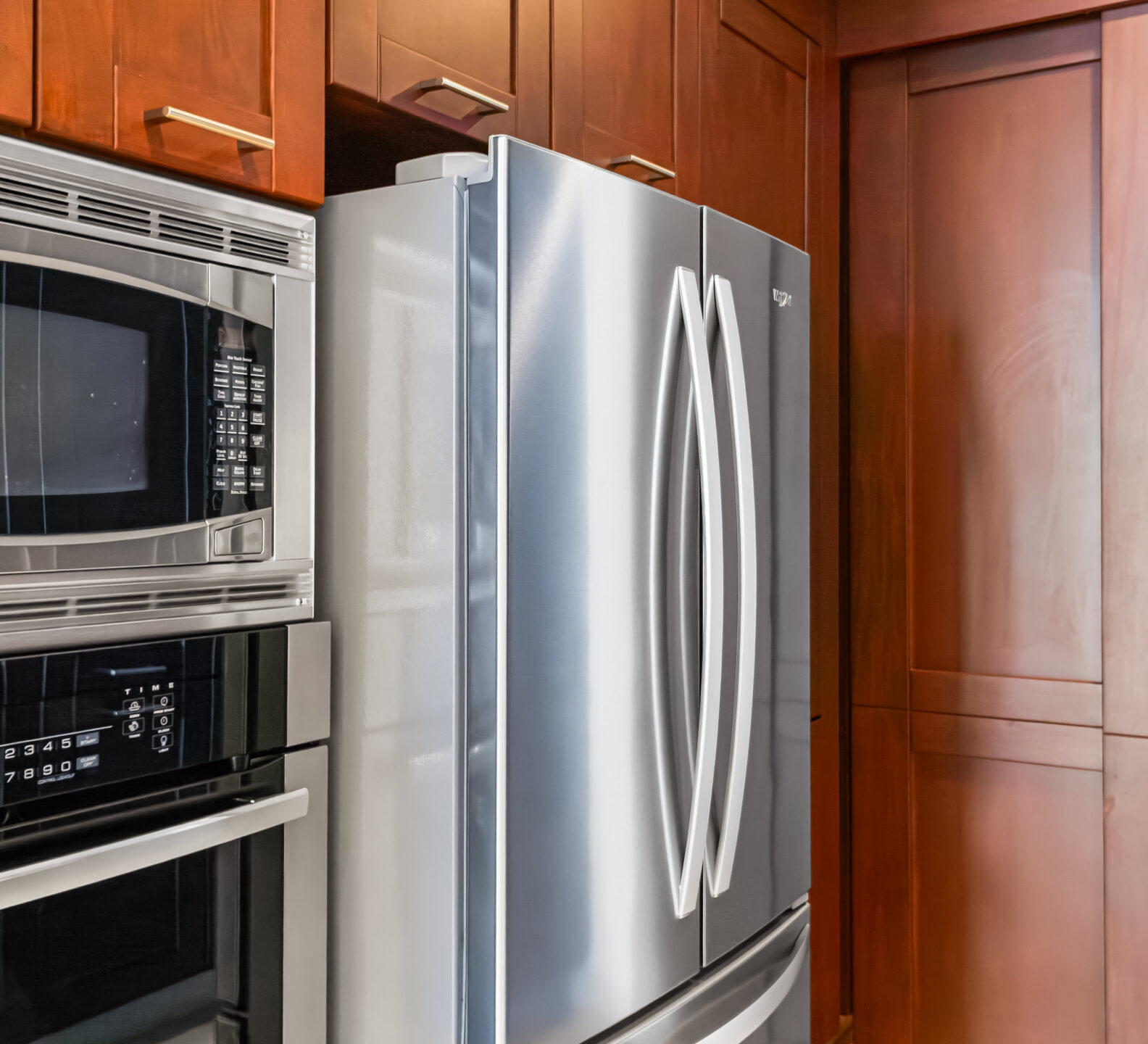 SDM Arco Major 4-12 Built-in stainless steel refrigerator and microwave framed by rich wood cabinetry in a contemporary kitchen setting.