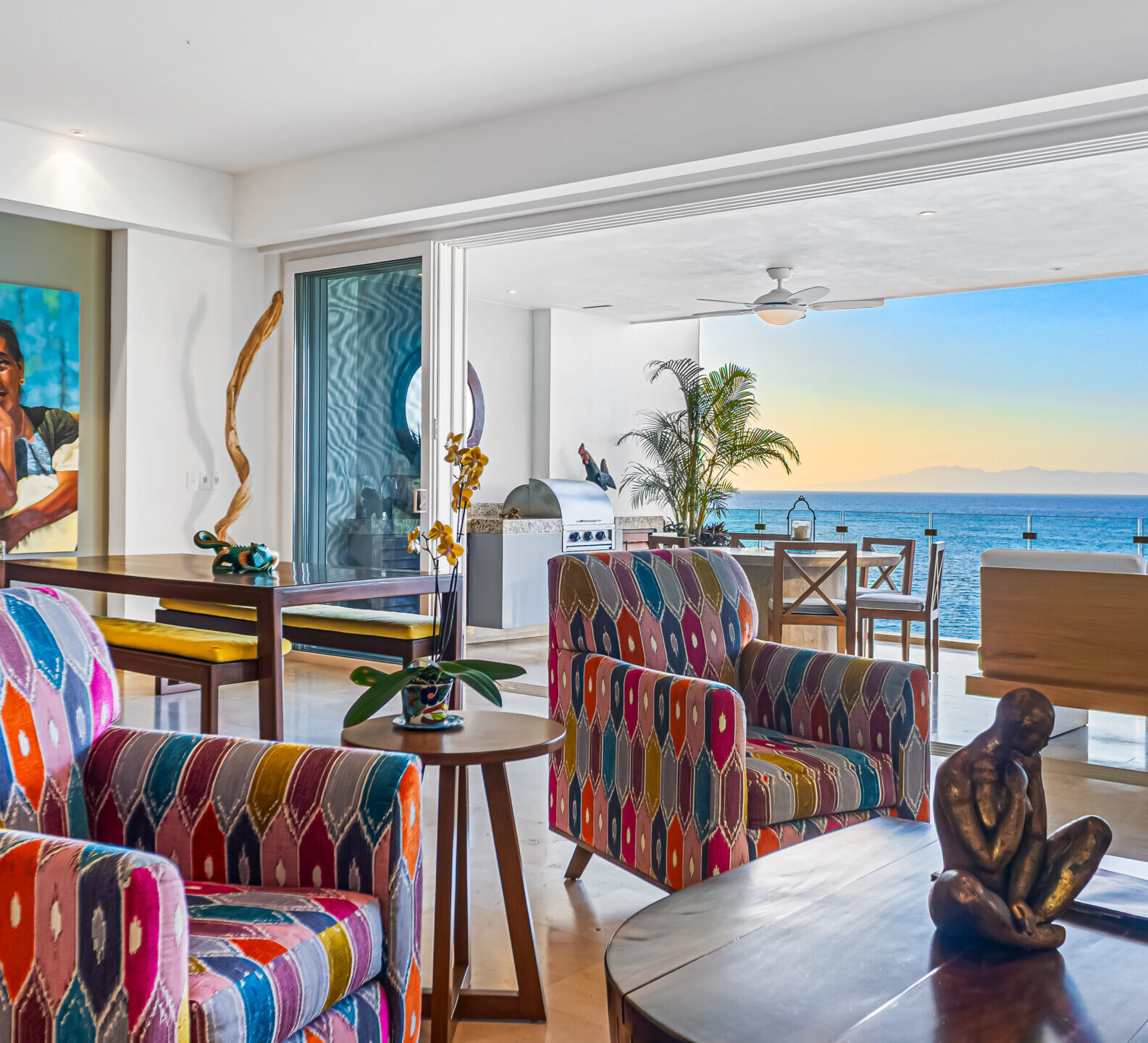 SDM Arco Major 4-15 Coastal-inspired dining and lounge area with vibrant upholstered chairs, decorative sculptures, and expansive ocean views through sliding glass doors.