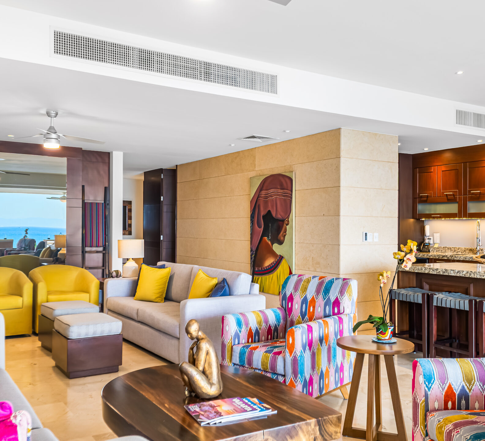 SDM Arco Major 4-18 Spacious open-concept living room and kitchen with colorful striped chairs, warm wood cabinetry, and contemporary artwork.