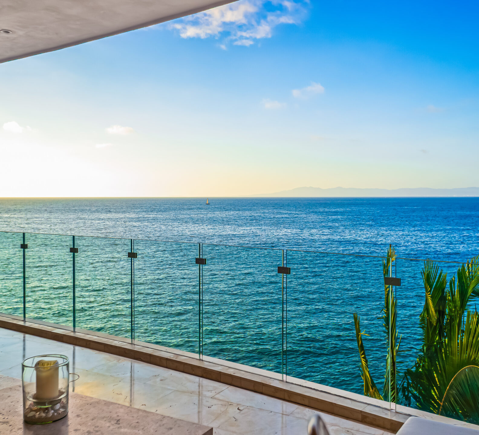 SDM Arco Major 4-35 Covered balcony with glass railings overlooking the blue ocean and distant coastline. Oceanfront Dining Table