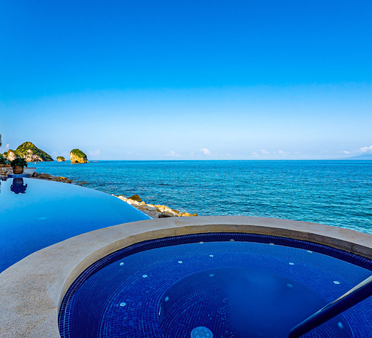 Infinity pool and circular spa overlooking the ocean under a clear blue sky.