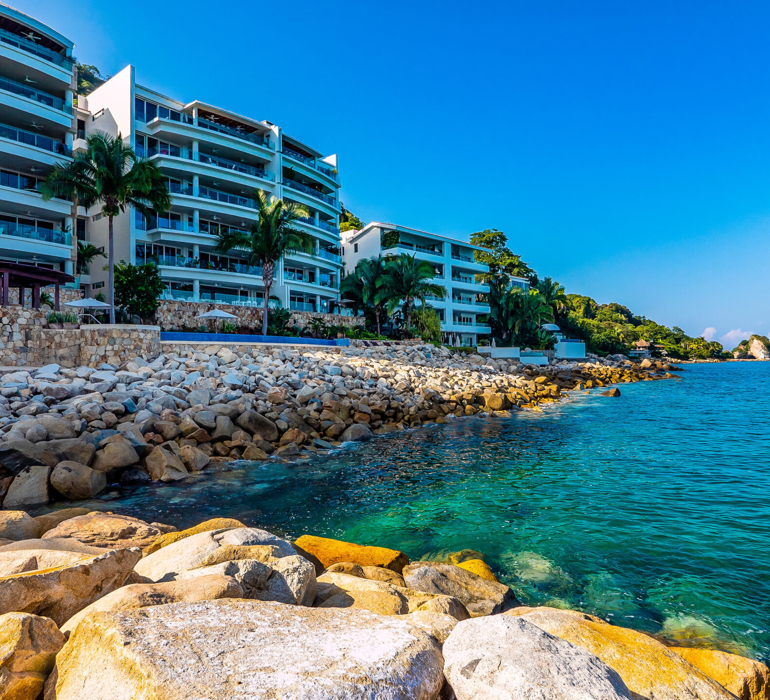 Oceanfront condominium buildings overlooking a rocky coastline and turquoise water.