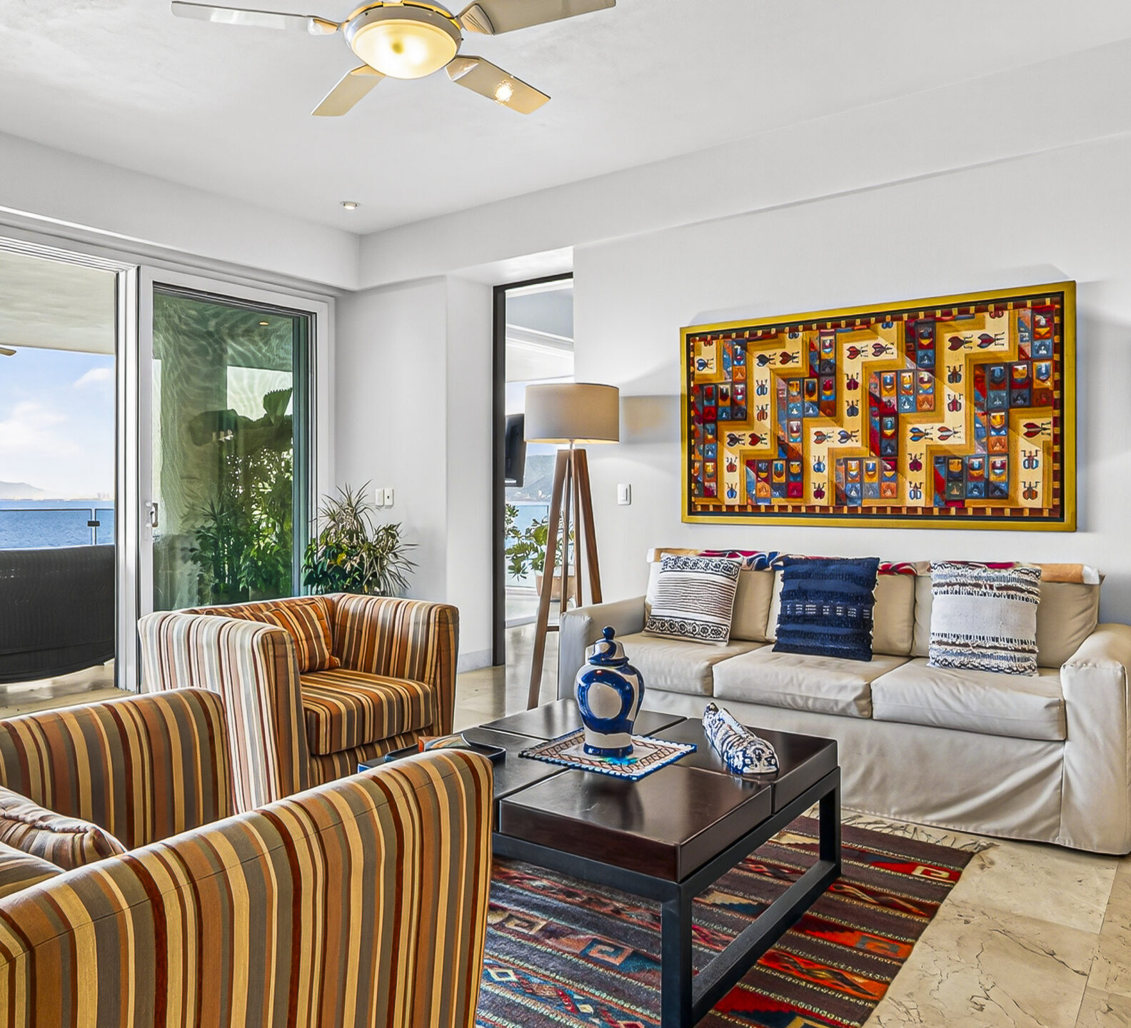 Living room with striped chairs, colorful artwork, and access to an oceanfront terrace.