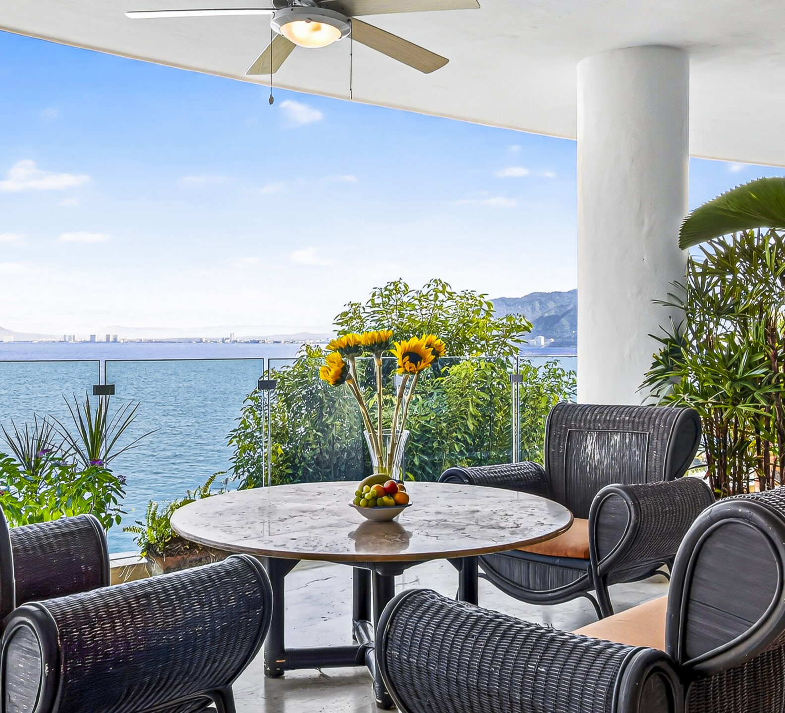 Covered oceanfront terrace with lounge chairs, a round table, and panoramic sea views.