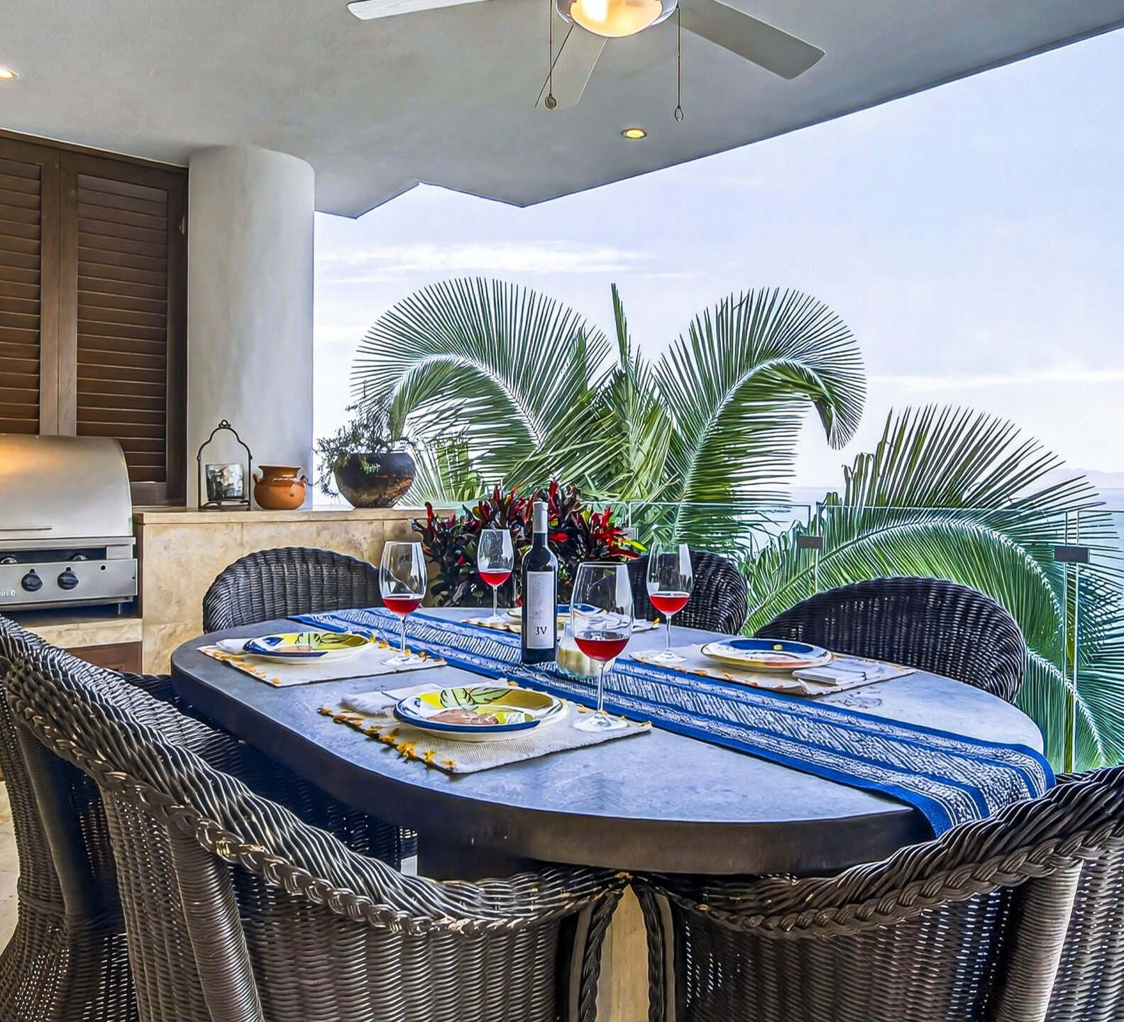 Outdoor dining table set for a meal on a covered terrace overlooking the ocean.