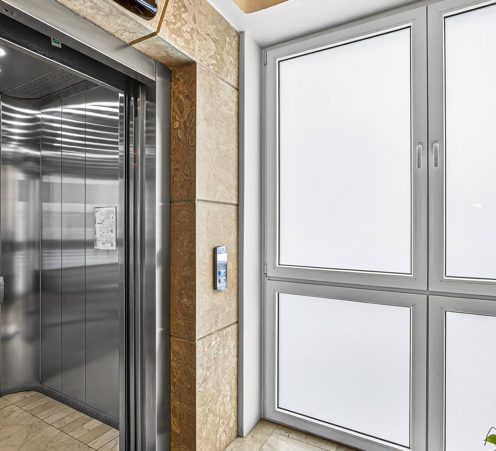 Modern elevator lobby with frosted glass doors and stone walls.