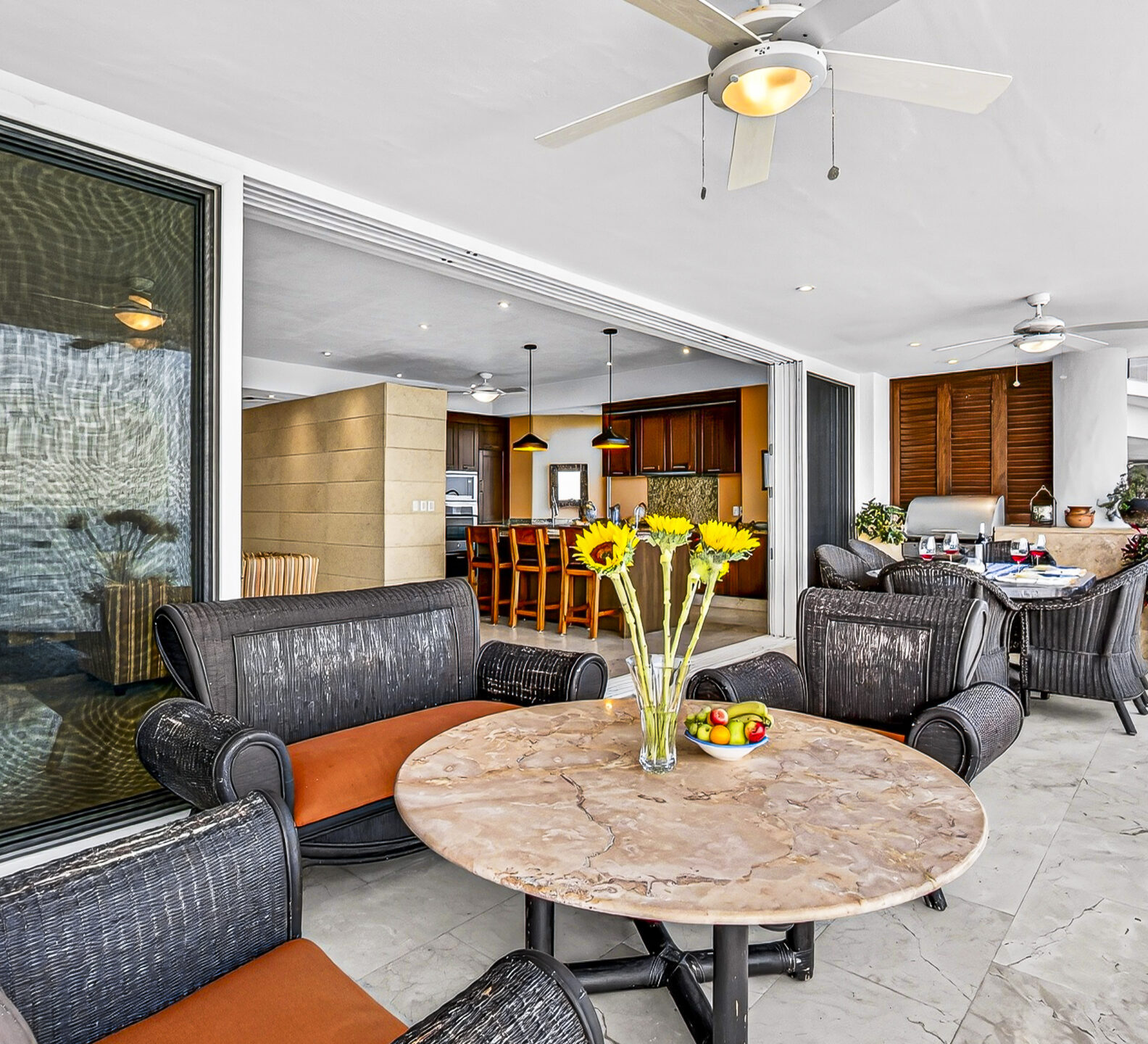 Covered terrace with wicker seating, a round table, and views into the living space.