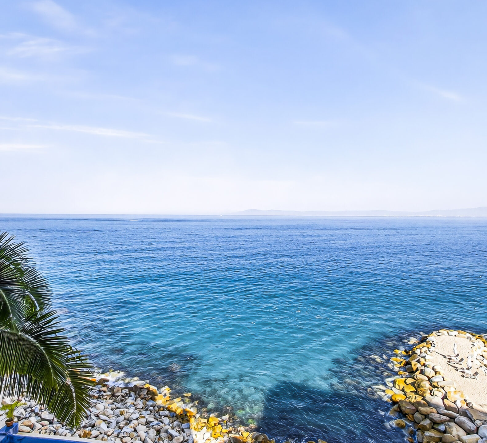 Expansive ocean view with turquoise water and rocky shoreline below.