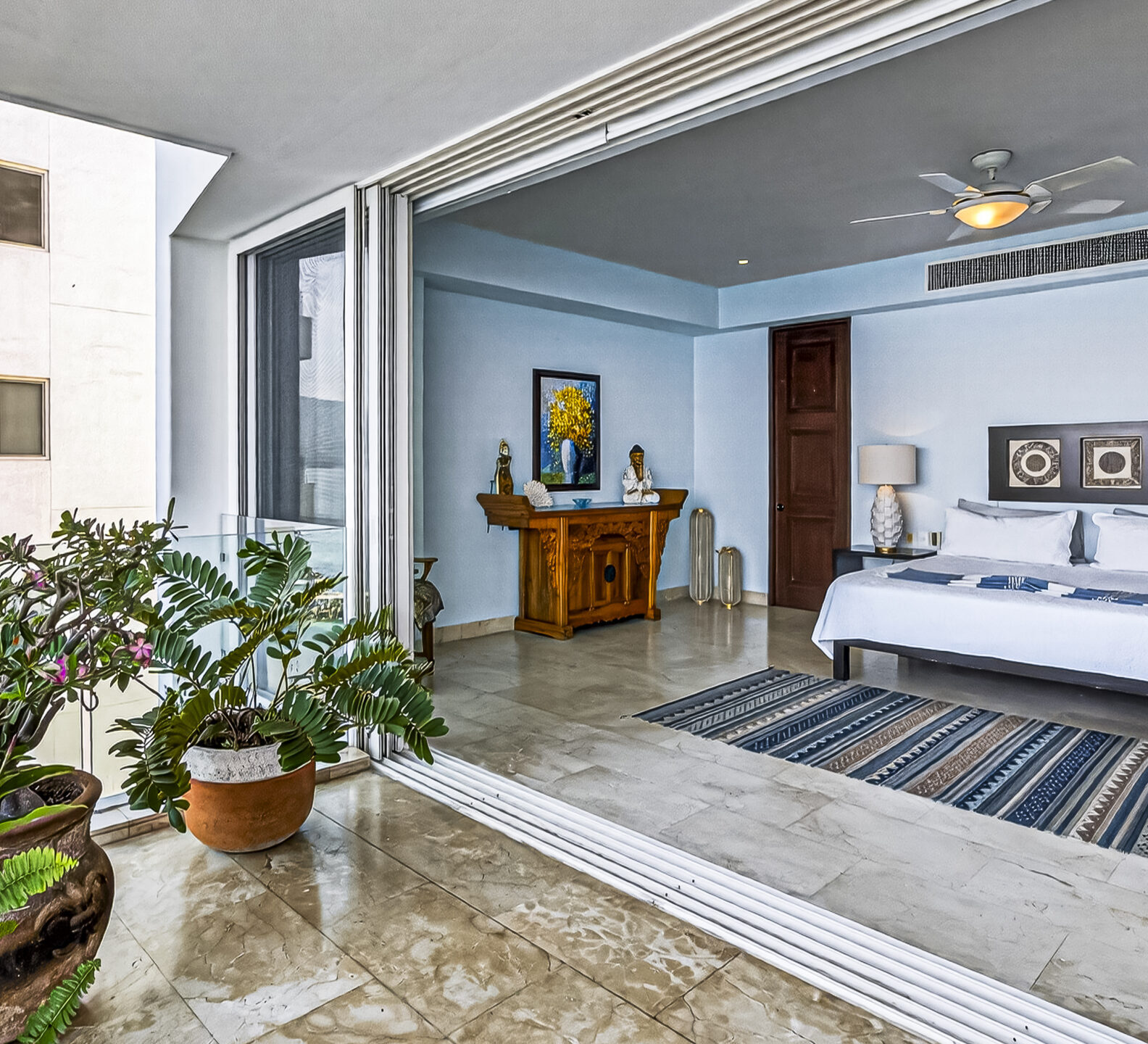 Bright bedroom with sliding glass doors opening to a private terrace with potted plants.