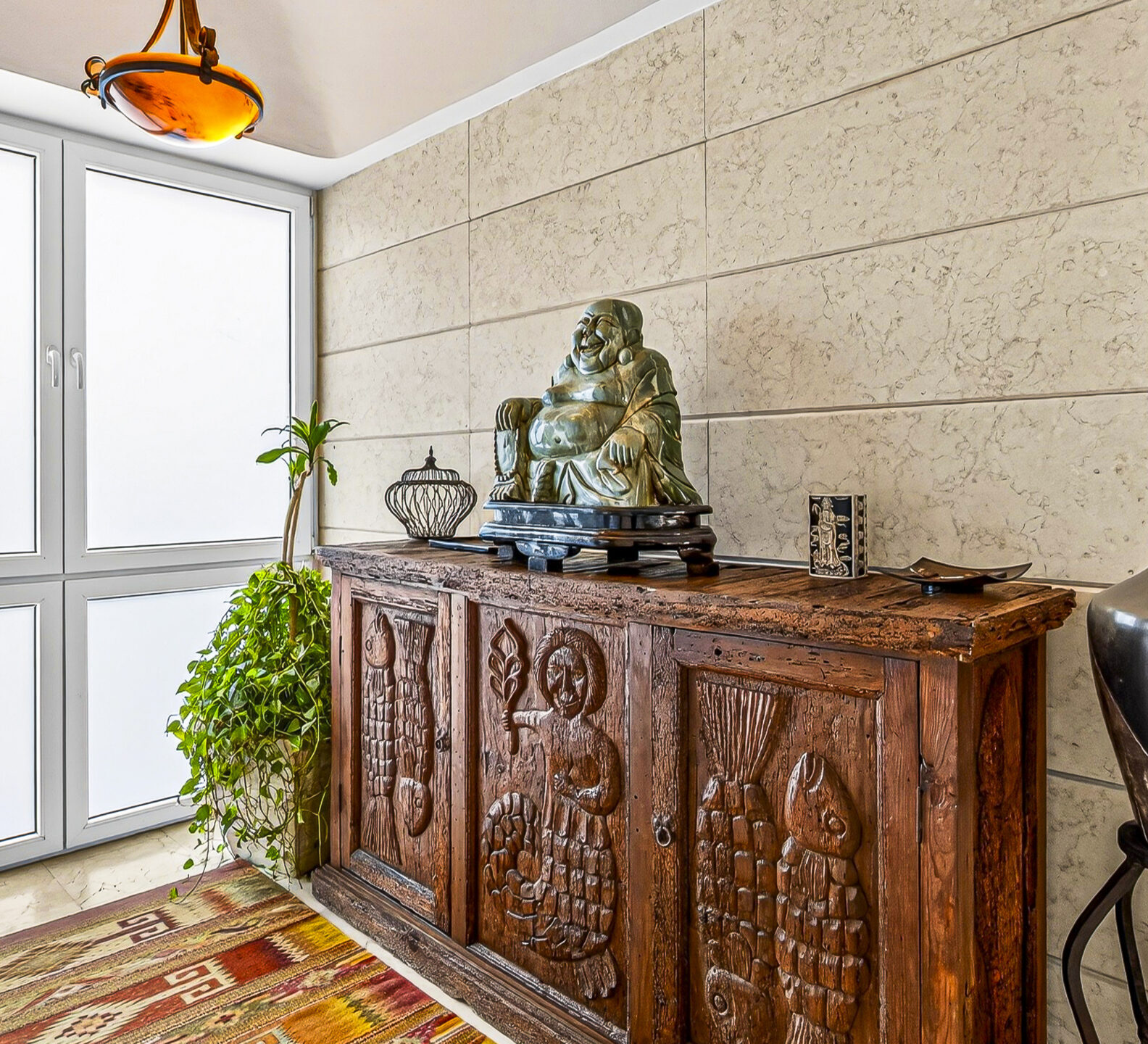 Entry area with a carved wood cabinet, decorative vase, and indoor plants.
