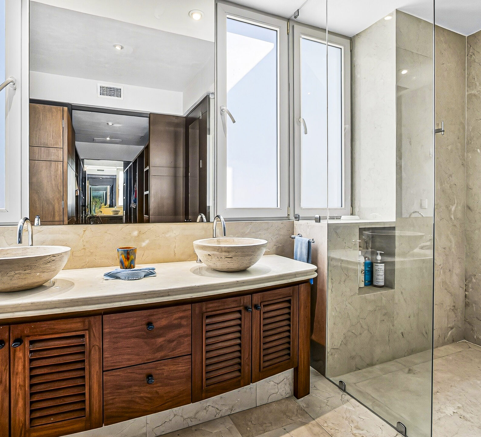 Bathroom with double vessel sinks, wood cabinetry, and a glass-enclosed shower.
