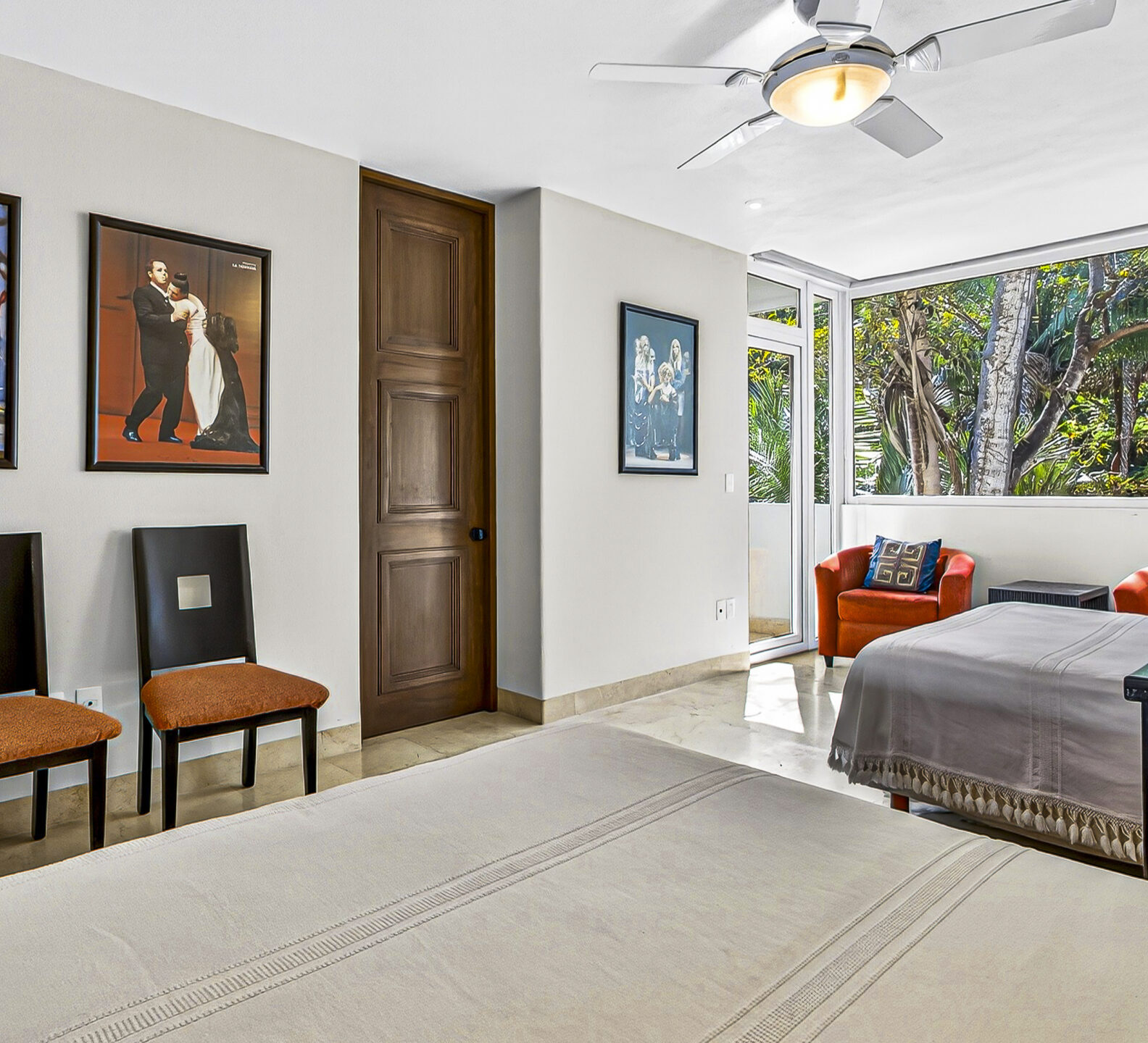 Guest bedroom with two beds, framed artwork, and large windows overlooking tropical greenery.