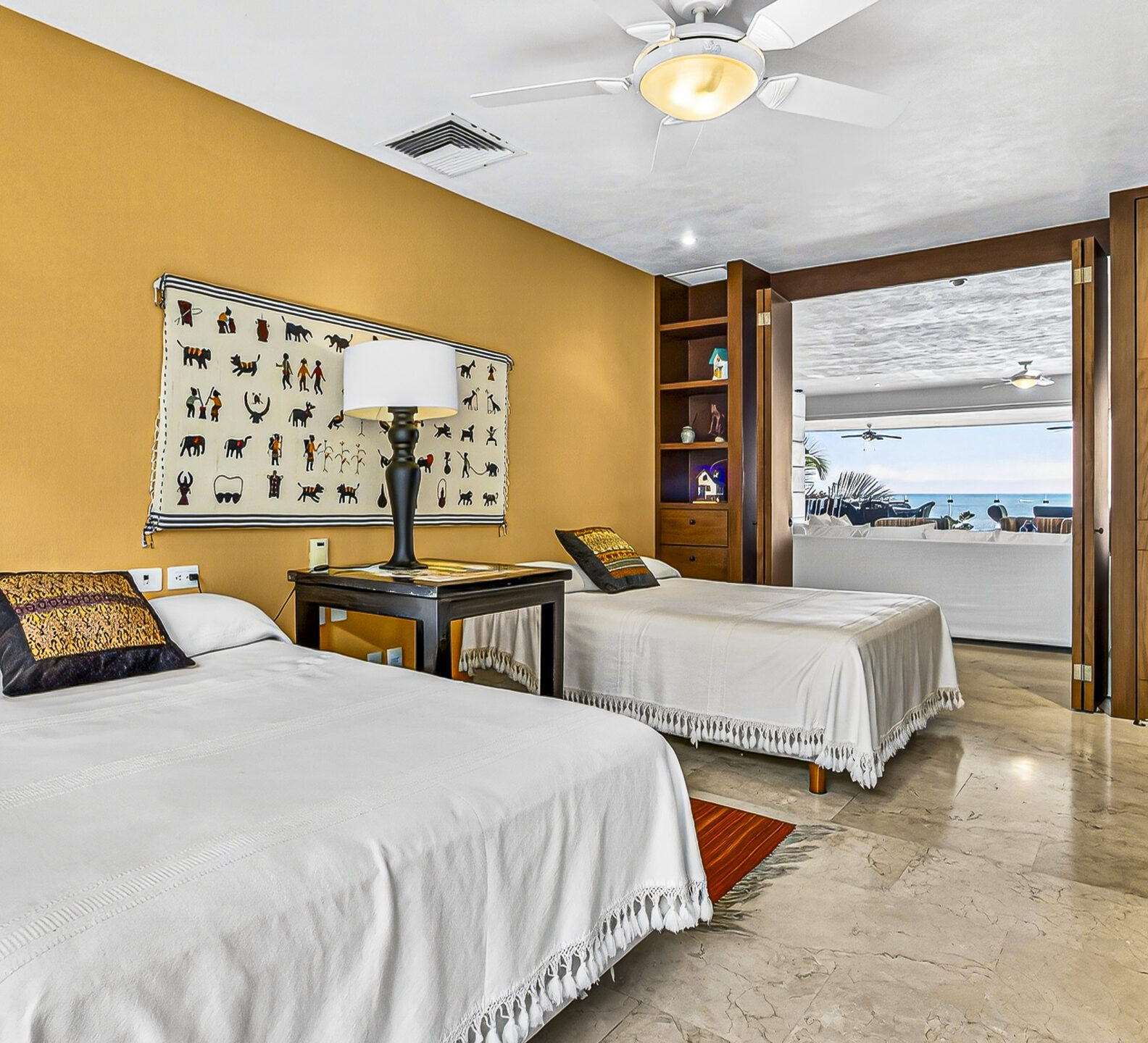 Bright bedroom with two twin beds, a desk, and louvered wood closet doors.