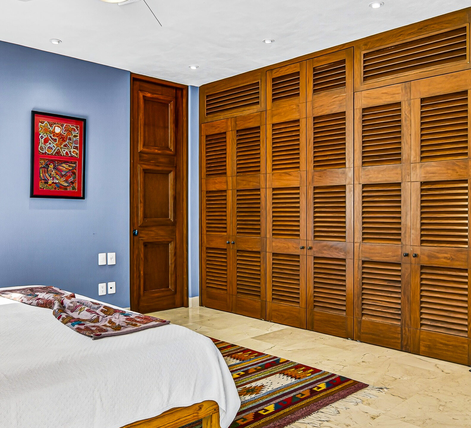 Bedroom with louvered wood closet doors and built-in shelving.