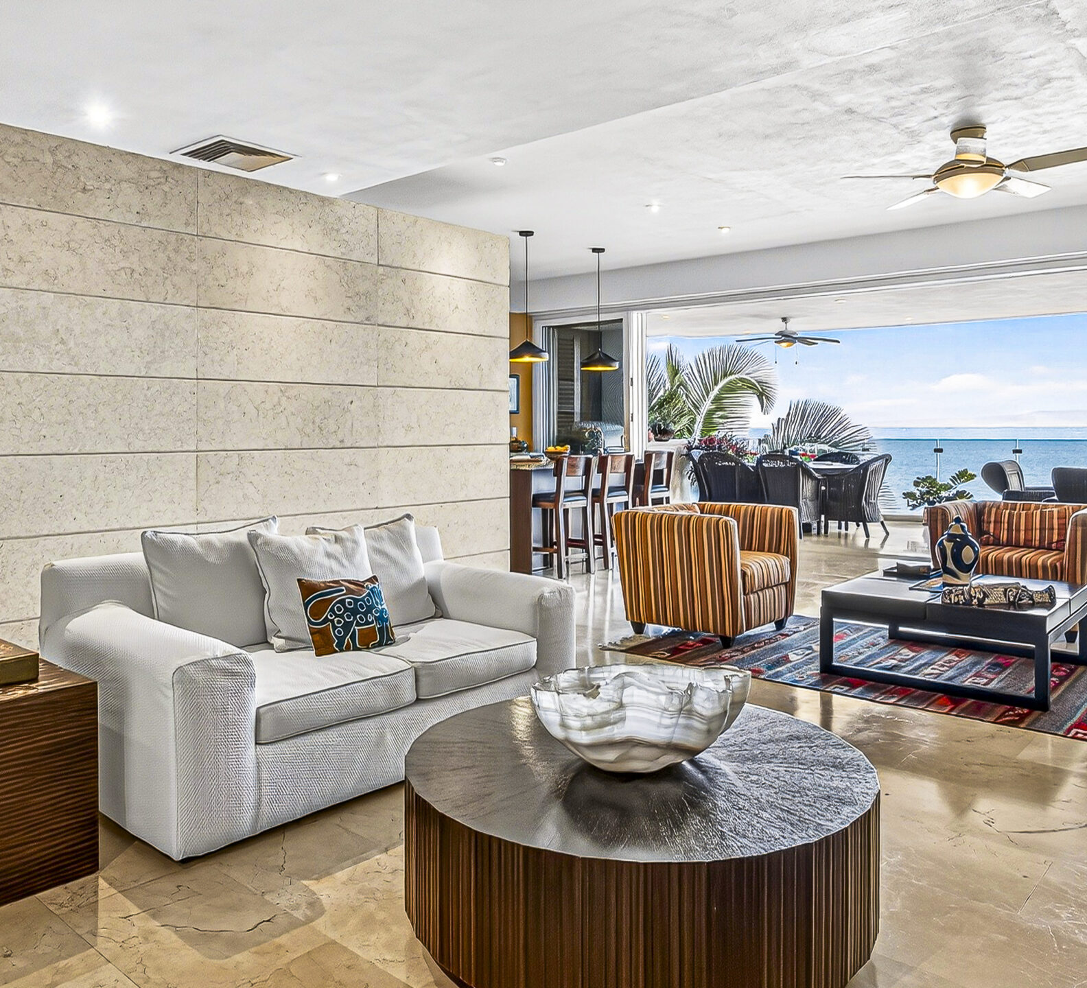 Open-concept living room with white sofas and sliding doors opening to an ocean-view terrace.