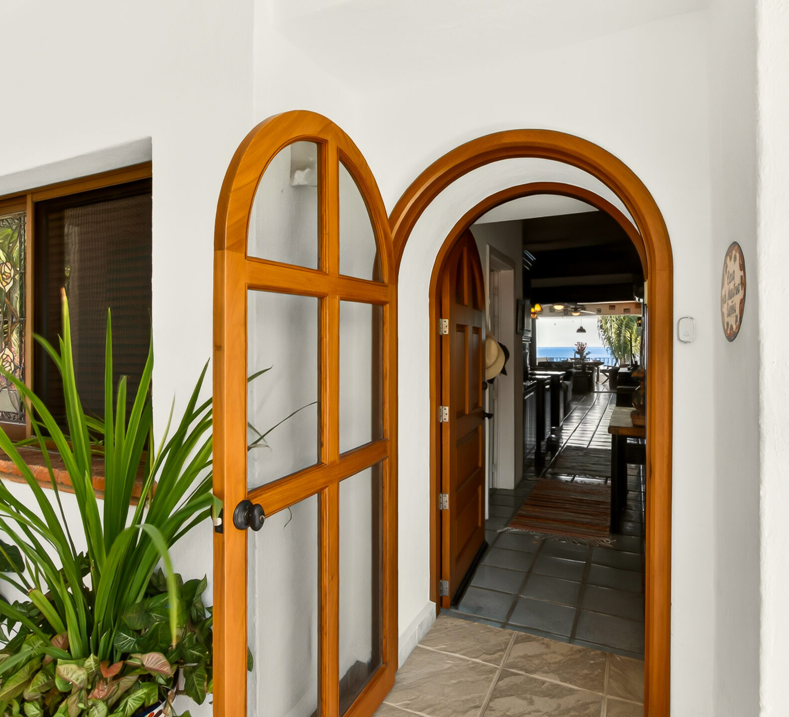 Welcoming entryway with arched wooden double doors, tropical plants, and a glimpse into the warm, inviting interior of the residence.
