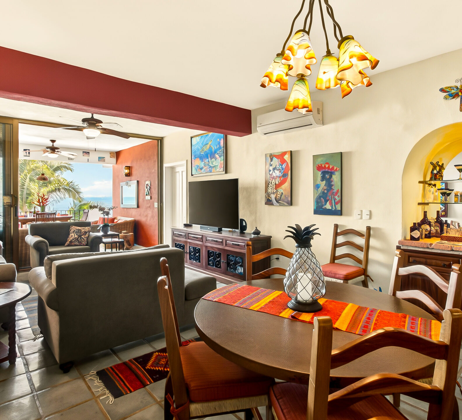 An open-concept living space featuring a central wooden dining table under an ornate light fixture, a dark sofa, and a built-in arched alcove.