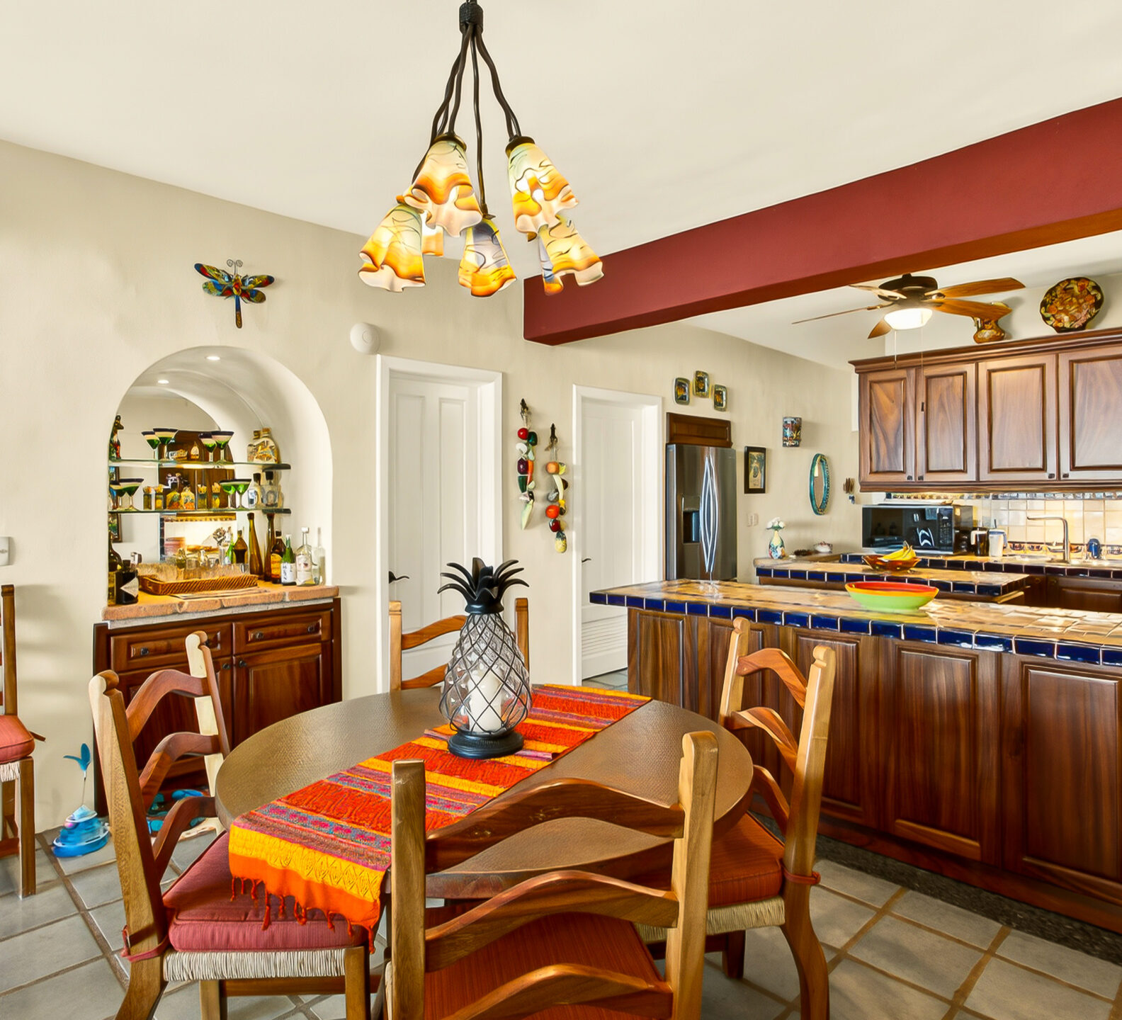 A view of a round wooden dining table positioned in front of a kitchen featuring dark wood cabinetry and a tiled breakfast bar.