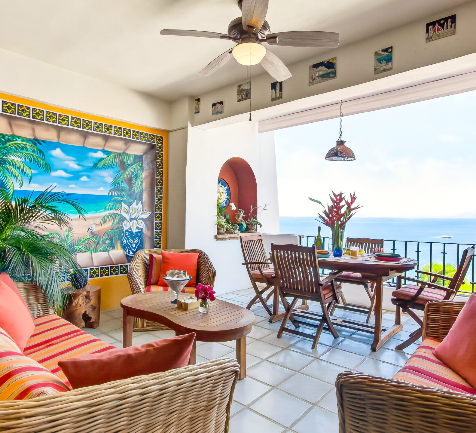 An outdoor patio featuring wicker seating with striped cushions and a dining table overlooking a scenic ocean view.