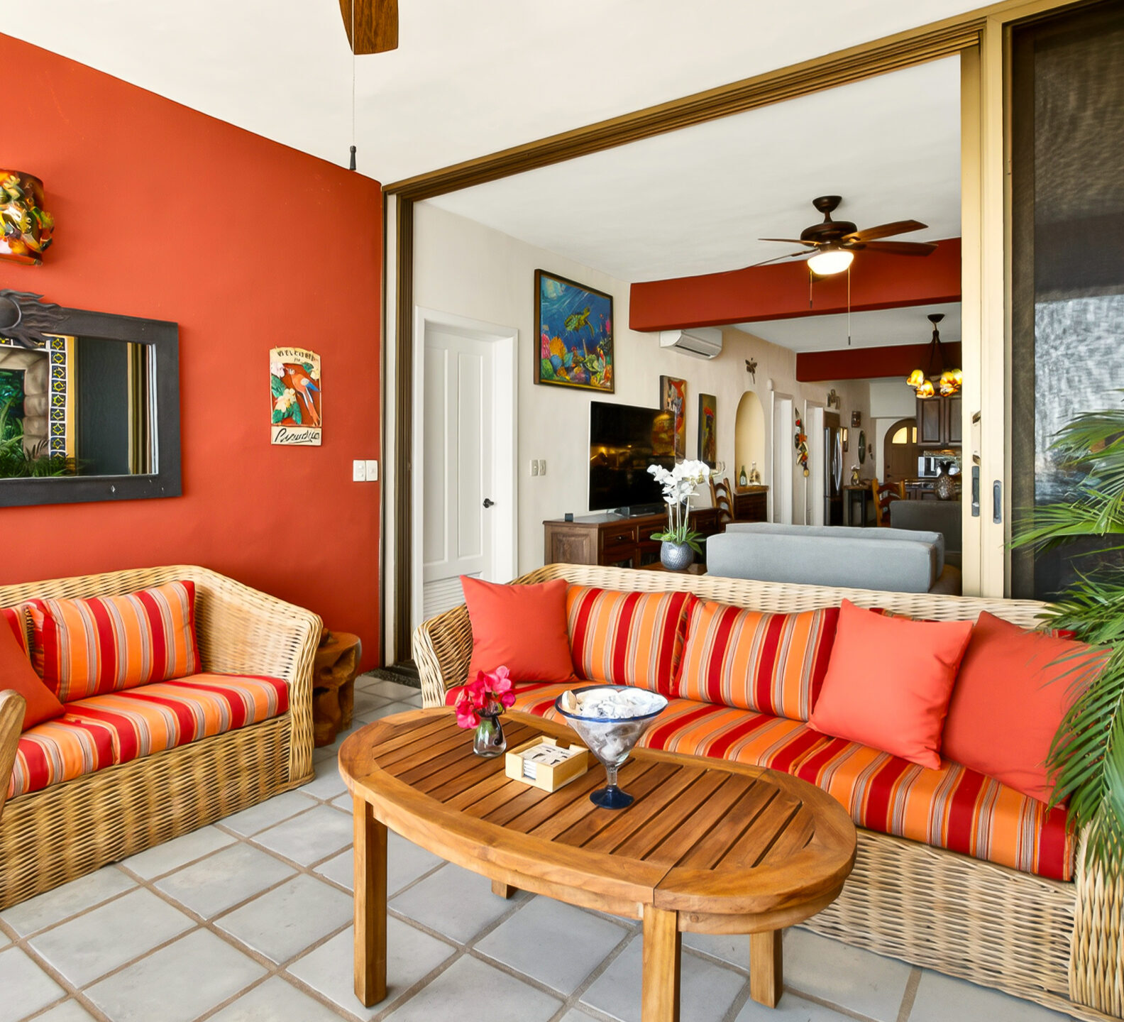A patio lounge area with wicker sofas, orange striped cushions, and an accent wall with a mirror reflecting the ocean view.