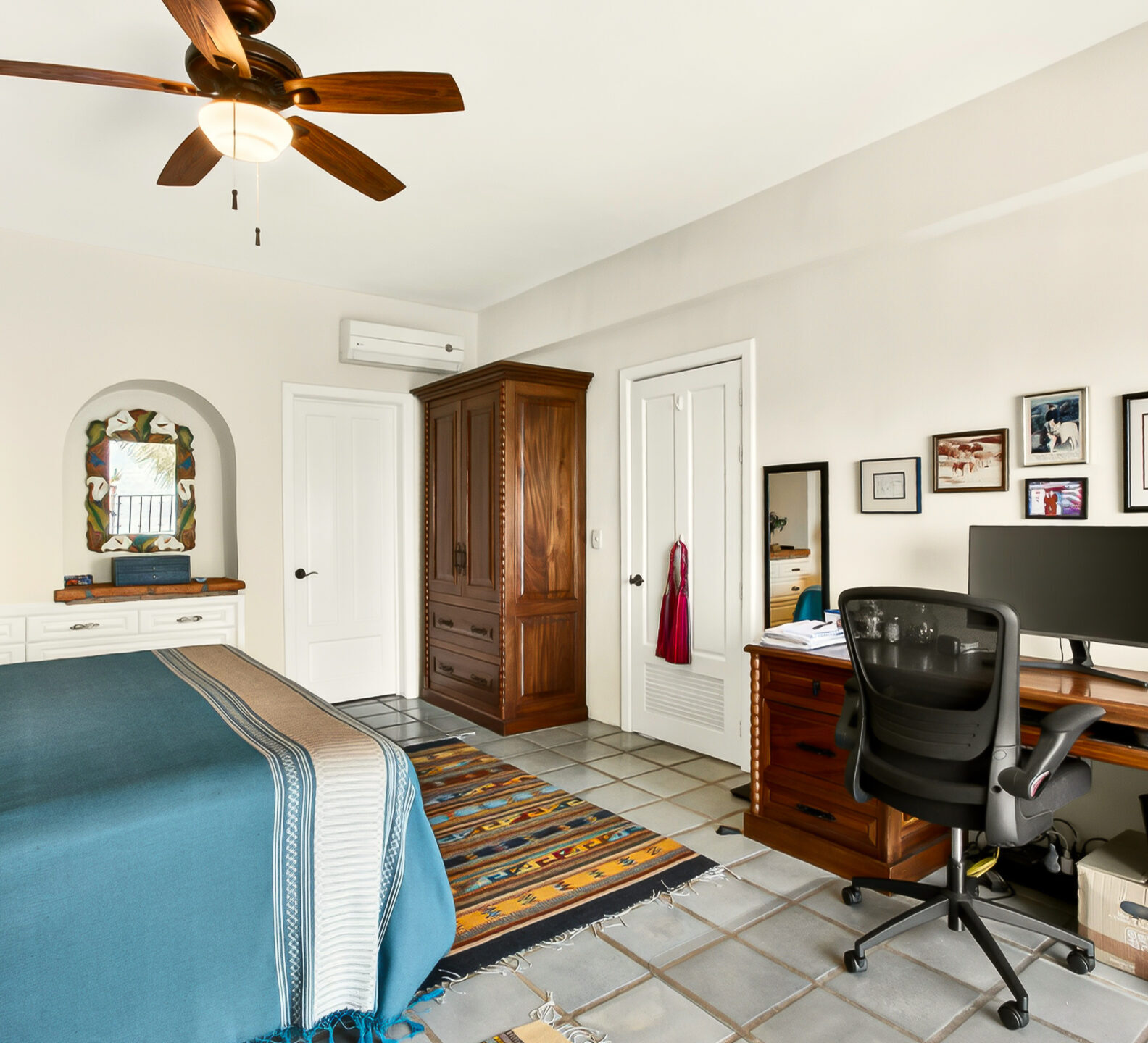 A bedroom perspective highlighting a wooden desk with a computer monitor, picture frames on the wall, and a large wooden wardrobe in the corner.