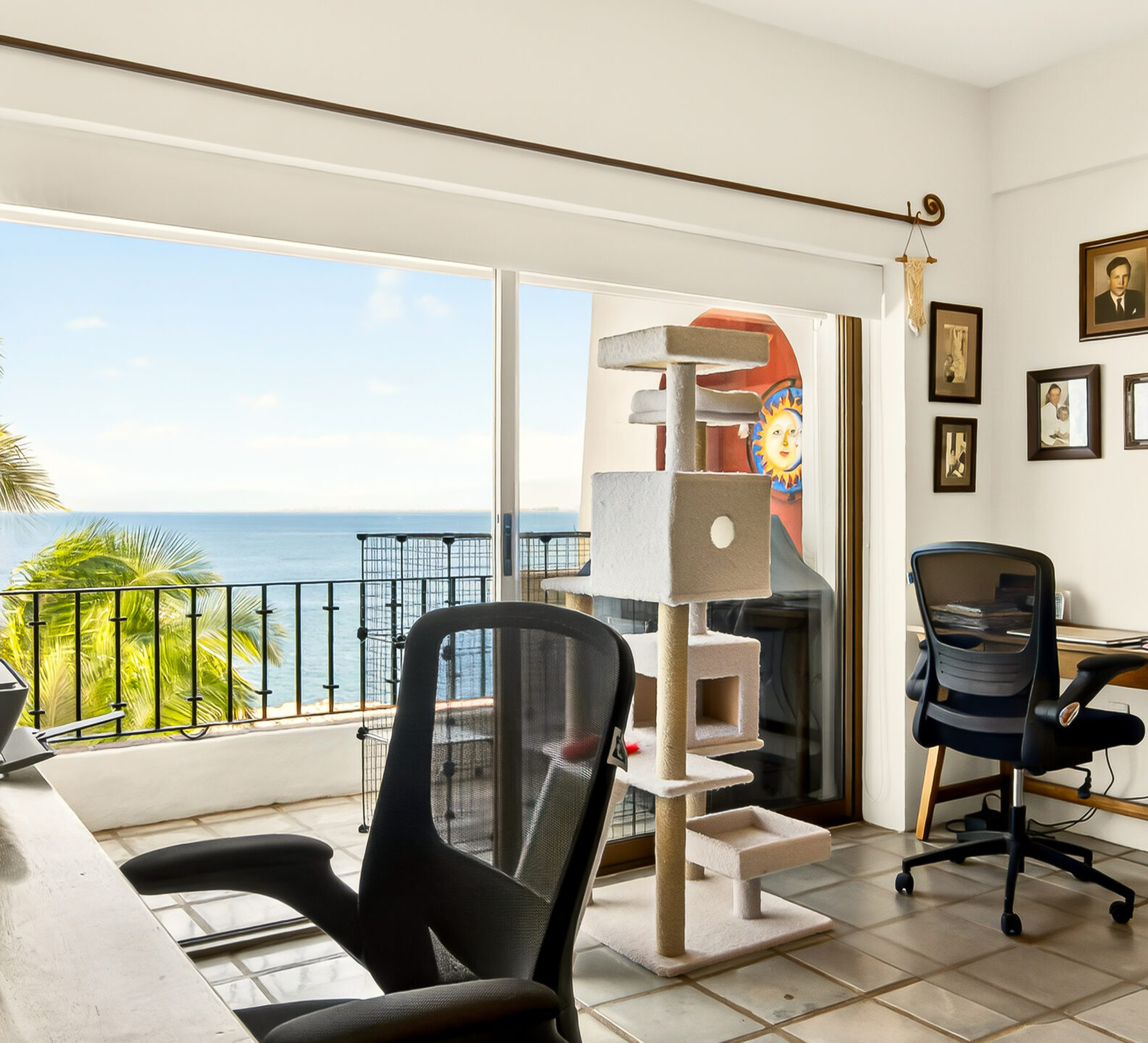 A bedroom home office area featuring dual wooden desks with black mesh chairs situated next to a large sliding glass door opening to an ocean-view balcony.