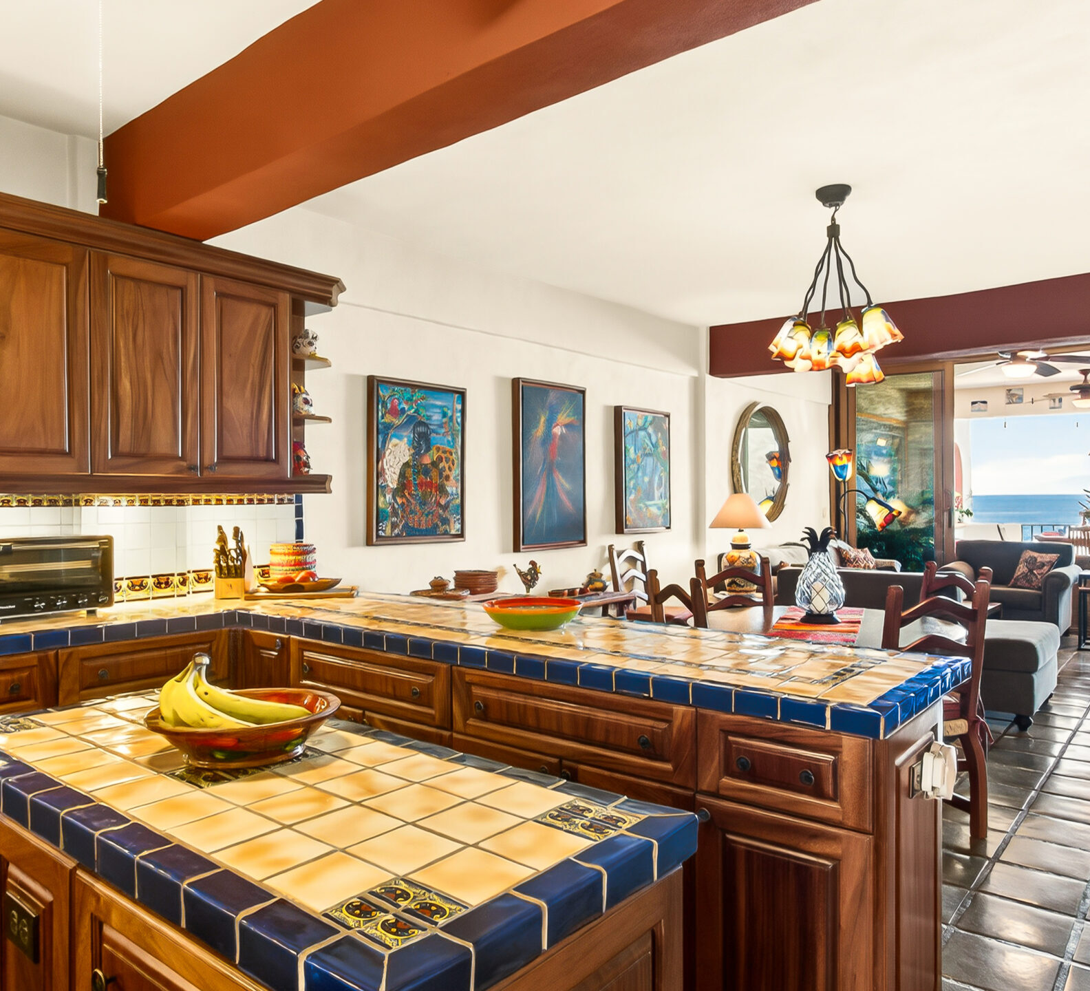 Spacious gourmet kitchen with handcrafted wood cabinetry, blue-tiled countertops, pendant lighting, and an adjacent dining area with ocean views.