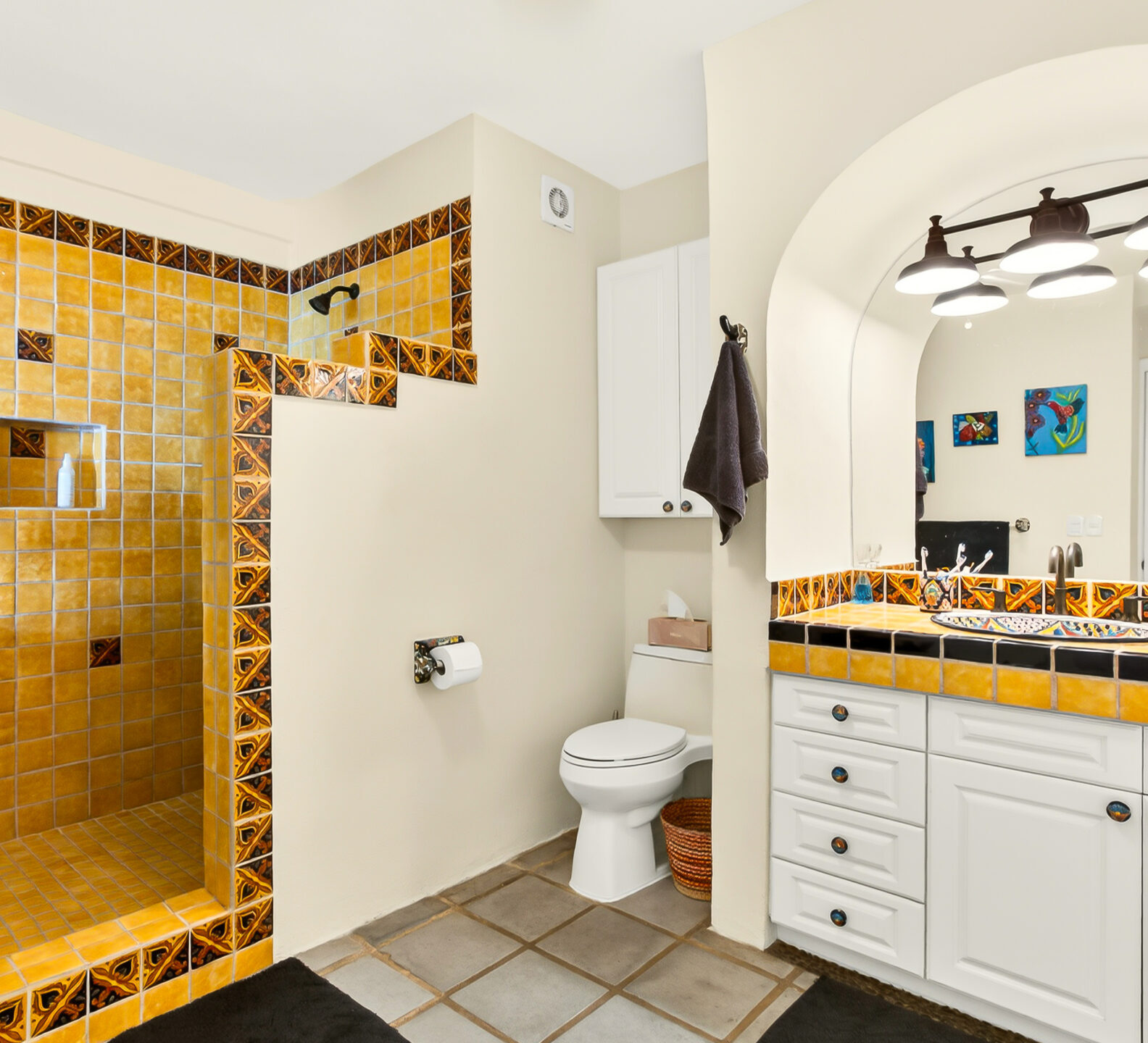 A bathroom featuring a walk-in shower with yellow-orange tiling, a toilet, and a white vanity with a large arched mirror.
