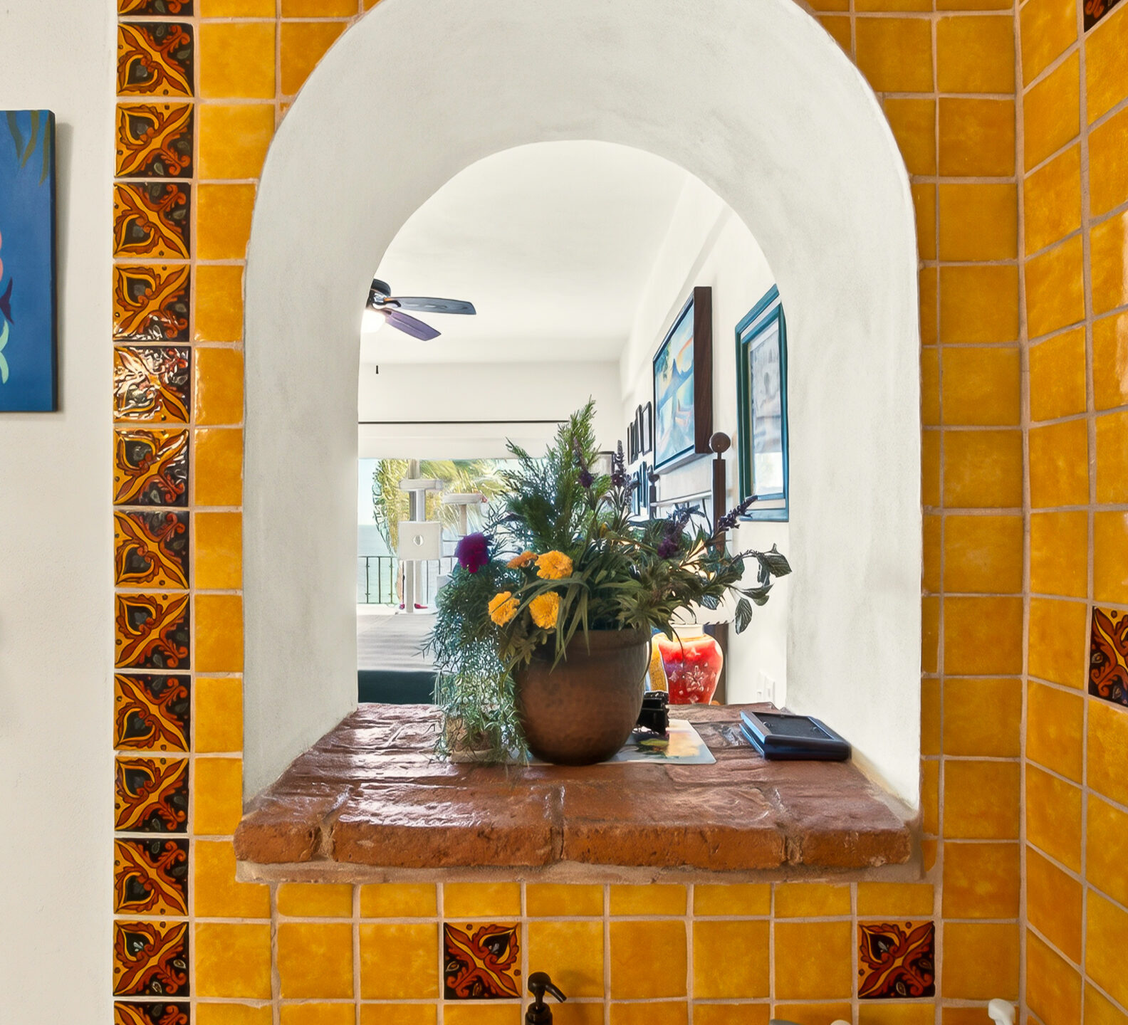 A close-up view of an arched window cutout framed by vibrant yellow-orange tiles, looking from the bathroom through to an adjacent room.