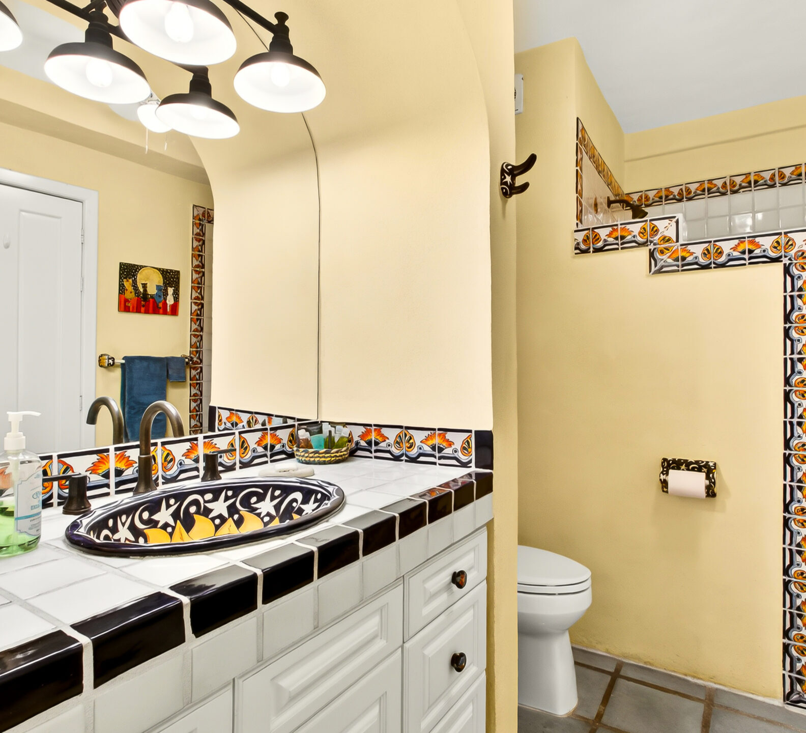 A bathroom view showing a white vanity with decorative black-and-white tile trim and a partial view of a tiled walk-in shower.