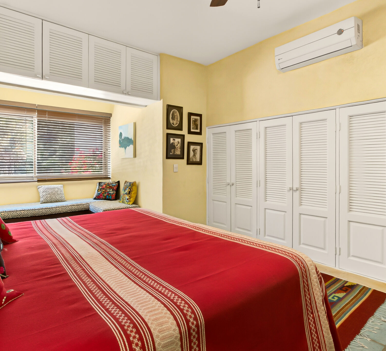 A perspective from the bed looking toward a large wall of white louvered closet doors and a wall-mounted air conditioner.