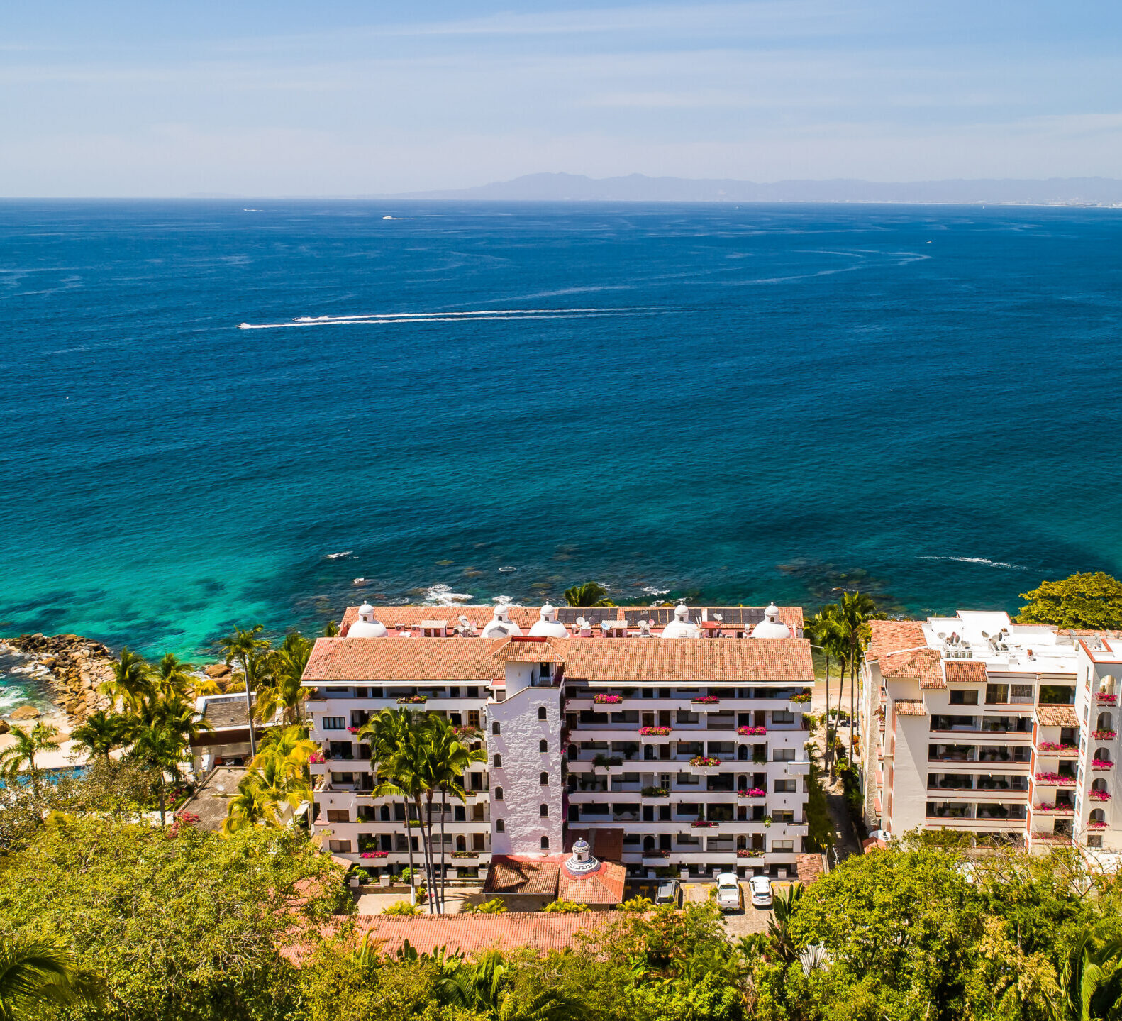 A high-angle aerial view captures beachfront resort complexes nestled in lush greenery along a deep blue ocean.