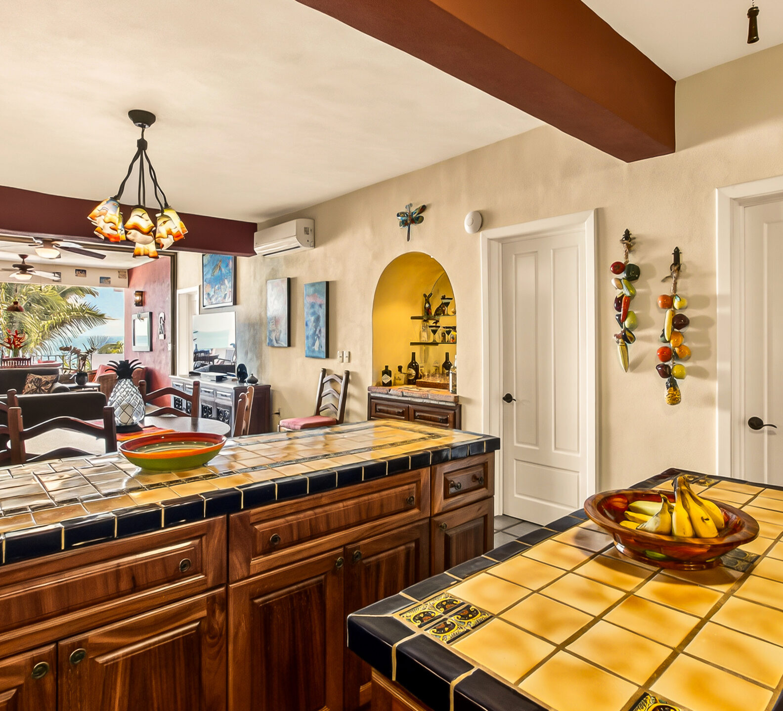 Kitchen island with yellow-tile counters reflecting in a large wall mirror, wood beam ceiling, and pendant light.